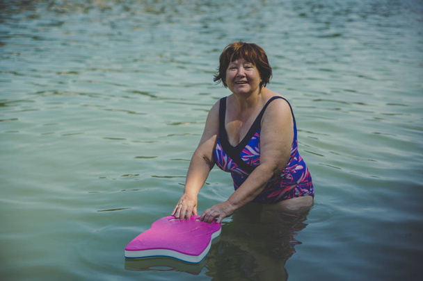 水中で水泳ボードを持つアクティブなシニア女性 - 写真・画像