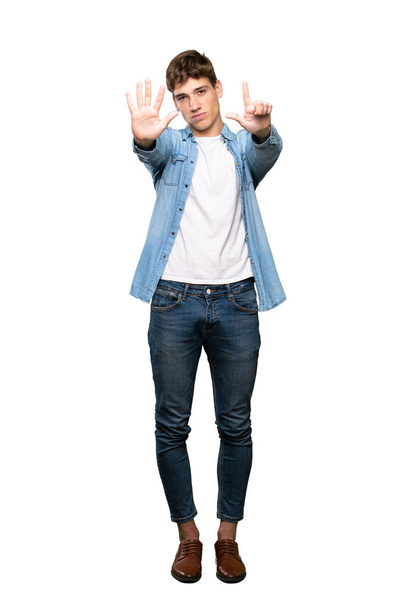 Een volledige foto van een knappe jongeman die zeven met vingers over een geïsoleerde witte achtergrond telt - Foto, afbeelding