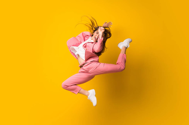 Young woman jumping over isolated yellow wall - Foto, afbeelding