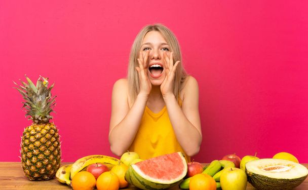 junge blonde Frau mit vielen Früchten schreit mit weit geöffnetem Mund - Foto, Bild