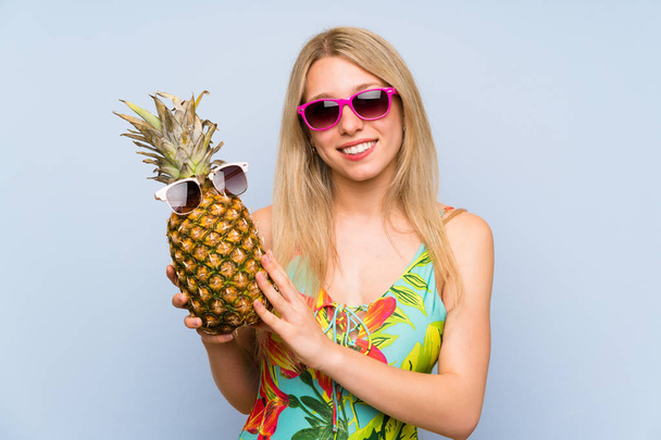 Young woman in swimsuit holding a pineapple with sunglasses - Foto, imagen