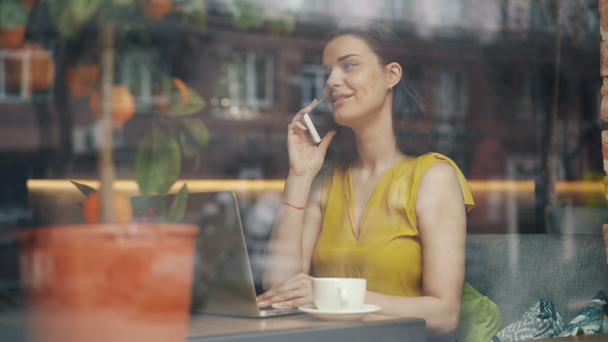 Menina falando no telefone celular e usando laptop sentado no café durante a pausa para o almoço
 - Filmagem, Vídeo