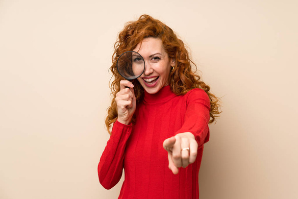 Redhead woman with turtleneck sweater holding a magnifying glass - Photo, image