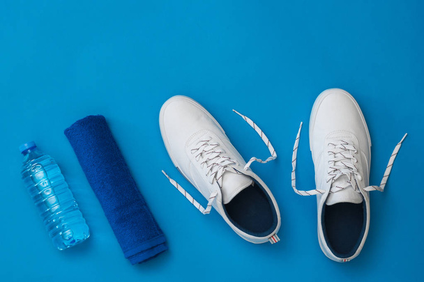 Witte Sneakers, een fles water en een blauwe handdoek op een blauwe achtergrond. Sport stijl. Platte lay. - Foto, afbeelding