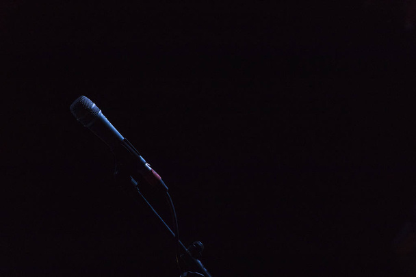 Microfono en su base, en fondo negro con luz que lo delinea - Фото, изображение