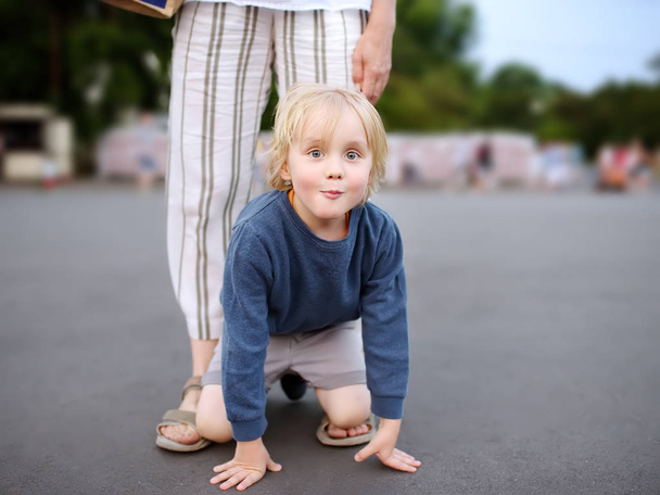 Mały zabawny chłopiec bawią się podczas chodzenia z matką. Dziecko oszukiwanie wokół ciepłego letniego wieczoru w parku publicznym. - Zdjęcie, obraz
