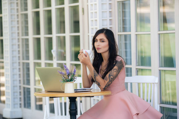 Beautiful girl freelancer drinks coffee in cafe, laptop and flowers on table - Zdjęcie, obraz
