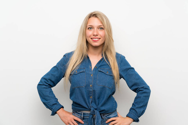 Young blonde woman over isolated white wall posing with arms at hip and smiling - Photo, Image