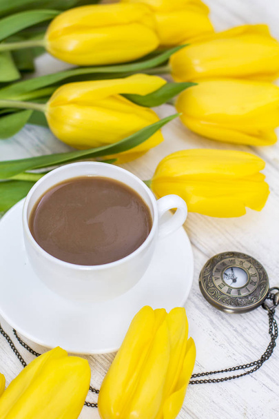 žluté tulipány, šálek kávy, cappuccino a staré hodinky na řetízku na bílém dřevěném pozadí - Fotografie, Obrázek