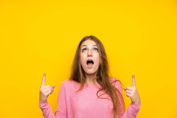 Young woman with long hair over isolated yellow wall surprised and pointing up - Photo, Image