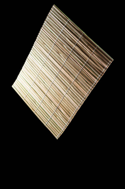 Мат для тарелок на столе из бамбука. Черный фон, изо
 - Фото, изображение