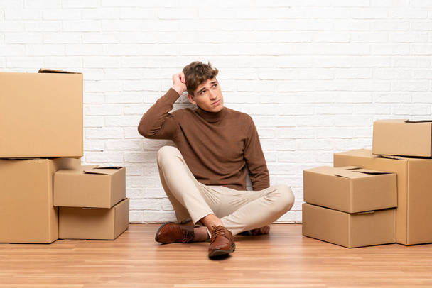Handsome young man moving in new home among boxes having doubts and with confuse face expression - Foto, Bild