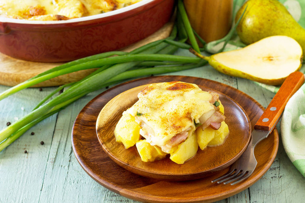 Potato gratin with pear, raclette cheese, and bacon on rustic wo - Photo, Image