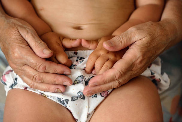 Old hands of grandmother holding baby on her laps. Family generation concept  - Foto, afbeelding