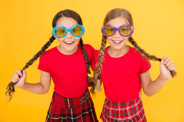 Summer accessory. Girls cute sisters similar outfits wear colorful sunglasses for summer season. Kids fashionable friends posing in sunglasses on yellow background. Summer fashion trend. Summer fun - Zdjęcie, obraz