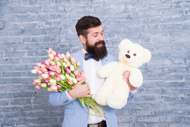 Romantic man with flowers and teddy bear. Romantic gift. Macho getting ready romantic date. Man wear blue tuxedo bow tie hold flowers bouquet. International womens day. Surprise will melt her heart - Photo, image