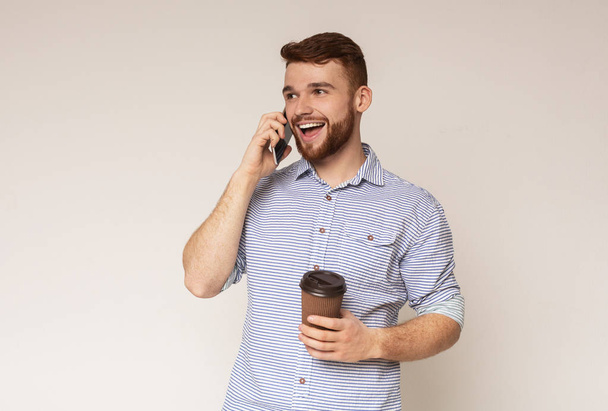 ハンサムなミレニアル世代の男は、携帯電話で話し、行くためにコーヒーを保持 - 写真・画像