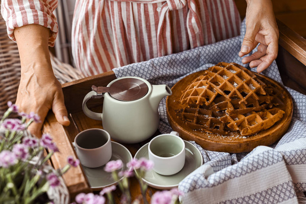 Women holds fresh baked waffles and tea mugs for breakfast. Morn - Zdjęcie, obraz