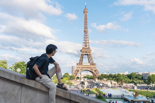 мужчина с рюкзаком смотрит на Эйфелеву башню, знаменитую достопримечательность и туристическое направление в Париже, Франция. Путешествие по Европе летом
 - Фото, изображение