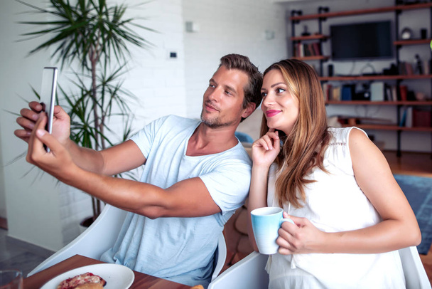 Happy couple having breakfast and take selfie together in the kitchen. - Photo, Image