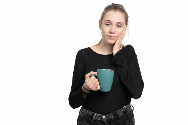 Μια νεαρή γυναίκα με ένα φλιτζάνι καφέ στο χέρι της είναι κουρασμένη. - Φωτογραφία, εικόνα