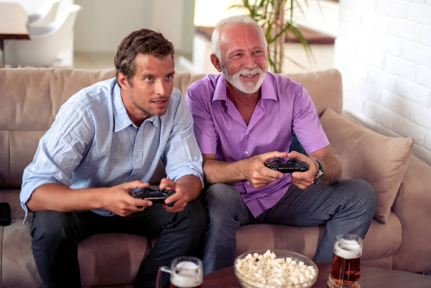 Πορτρέτο δύο ενθουσιασμένων ανδρών που παίζουν βιντεοπαιχνίδι στο σπίτι. - Φωτογραφία, εικόνα