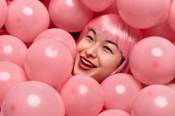 Cheerful Asian female in heap of balloons - Foto, Bild