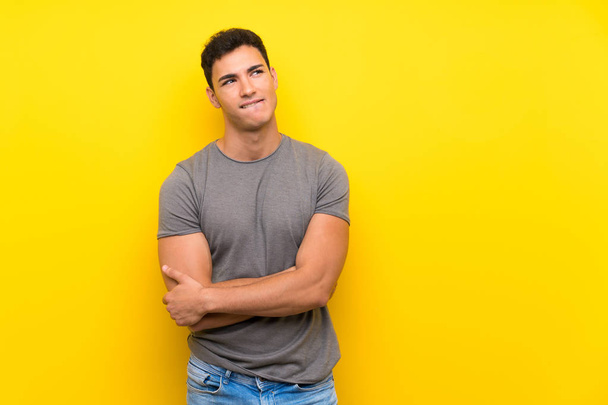 Hombre guapo sobre pared amarilla aislada con expresión de cara confusa
 - Foto, imagen