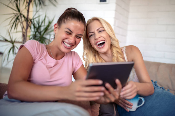 Ευτυχισμένες νεαρές φίλες που χρησιμοποιούν tablet στο σπίτι. - Φωτογραφία, εικόνα