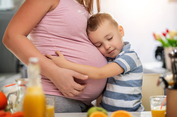 Madre embarazada y su hijo disfrutando en la cocina y haciendo jugo de naranja fresco. - Foto, imagen