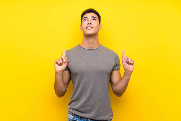 Handsome man over isolated yellow wall surprised and pointing up - Photo, Image