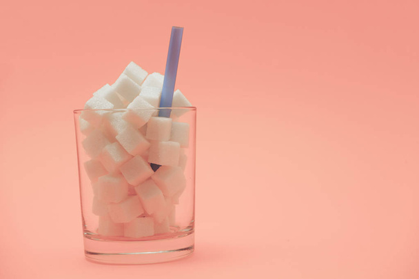 Glass full of cubes sugar with straw on a beautiful peach  background  - unhealthy diet concept. - 写真・画像