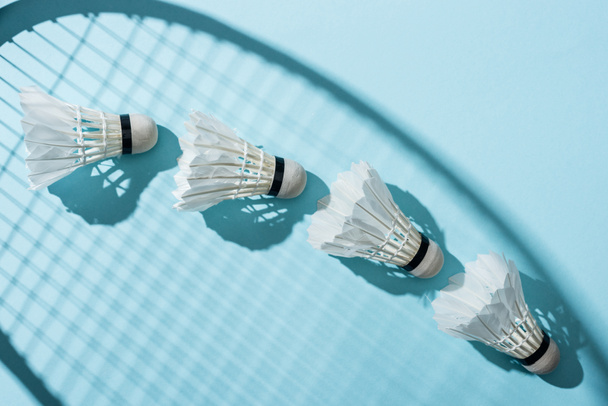 top view of shuttlecocks near shadow of badminton racket on blue  - 写真・画像