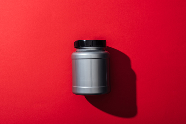 top view of grey plastic jar with protein on red  - Fotografie, Obrázek