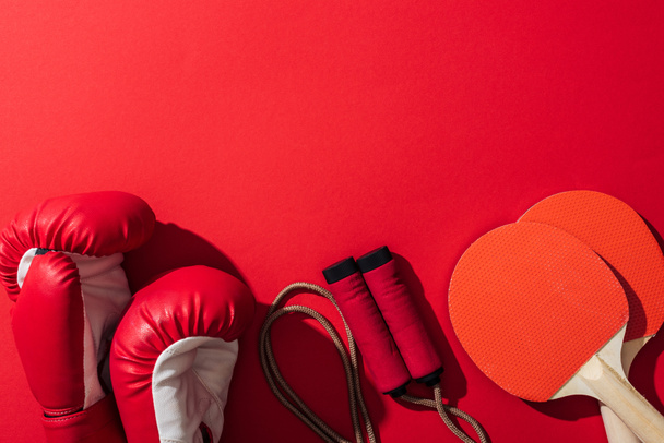 top view of boxing gloves near red ping pong rackets and skipping rope on red  - Photo, Image