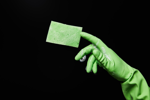 обрізаний вид людини в зеленій гумовій рукавичці з губкою на чорному тлі
  - Фото, зображення