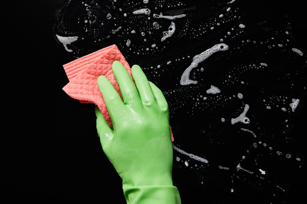 bijgesneden beeld van de man in rubber handschoen schoonmaken met roze Rag op zwarte achtergrond  - Foto, afbeelding