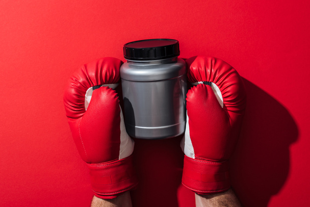 cropped view of man holding grey jar in boxing gloves on red   - Foto, Imagen