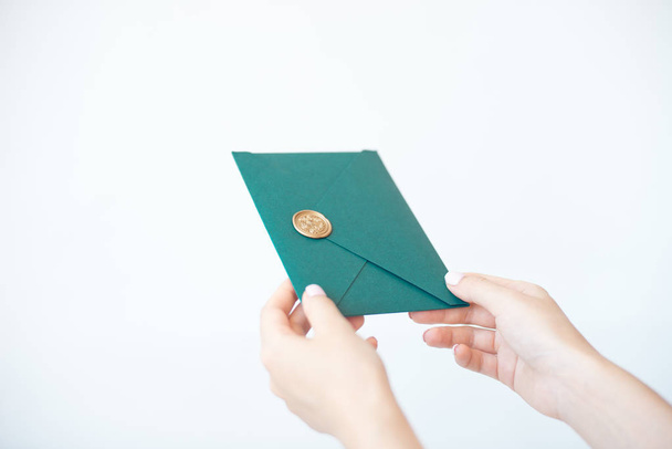 Balmumu mührü, hediye çeki, kartpostal, düğün davetiyekartı ile yeşil davetiye zarfı tutan kadın ellerinin yakın çekim fotoğrafı. - Fotoğraf, Görsel