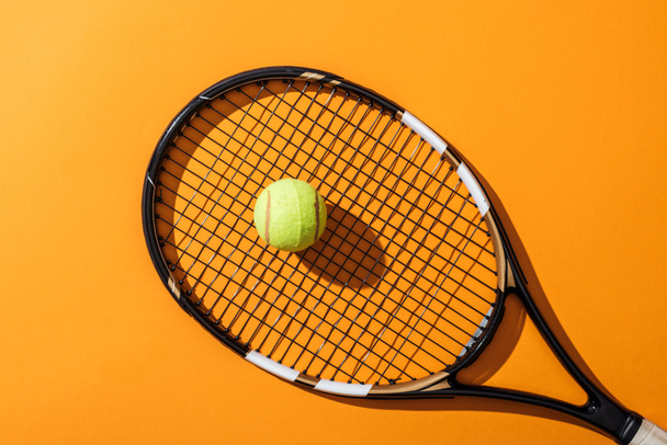top view of tennis racket near green tennis ball on yellow  - 写真・画像