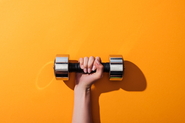 cropped view of woman holding heavy dumbbell while exercising on yellow  - Photo, Image