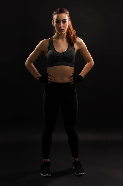 Full length of confident female athlete standing with hand on hip against plain background - Photo, Image
