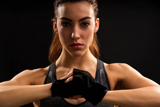 Portrait of young Caucasian woman punching her palm with fist against black background - Foto, Imagen