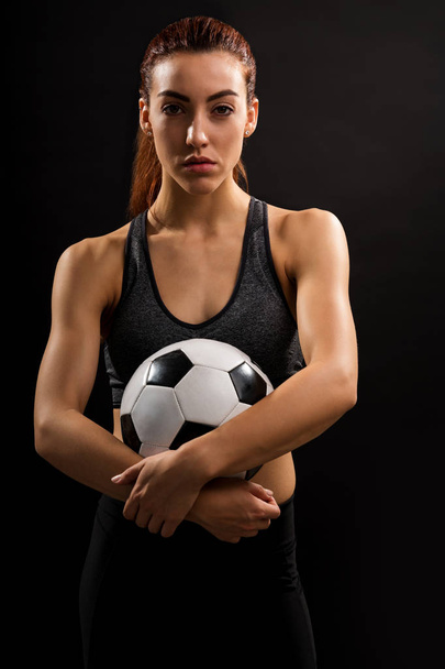 Retrato de una joven y bonita jugadora sosteniendo pelota de fútbol sobre fondo negro
 - Foto, Imagen