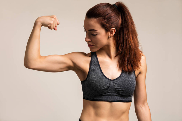 Beautiful female athlete flexing muscles while standing against brown background - Photo, image
