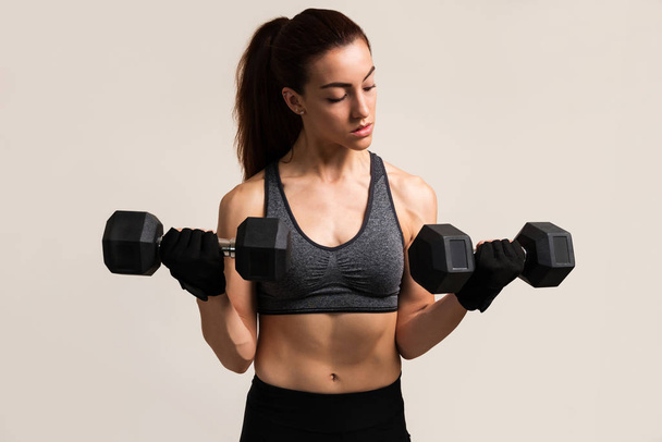 Female athlete lifting dumbbells against brown background - Photo, Image