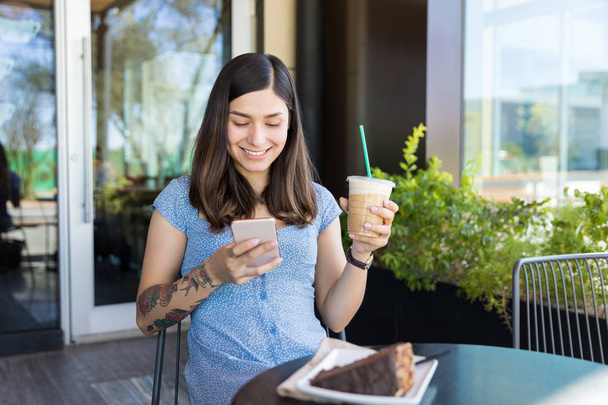 Χαμογελαστά επηρεάζων μηνύματα στο κινητό τηλέφωνο, ενώ έχετε καφέ στο καφέ - Φωτογραφία, εικόνα
