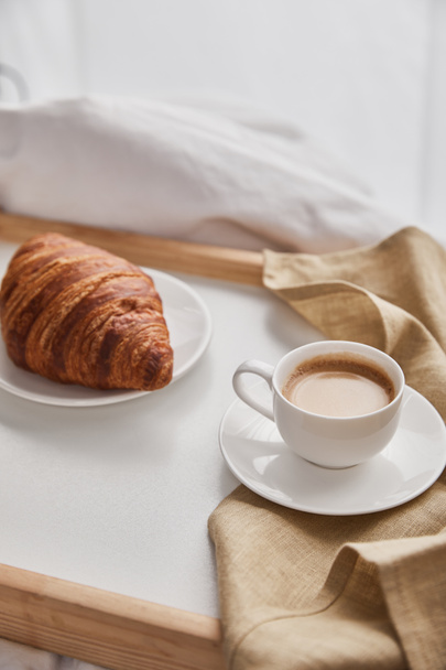 fresh croissant on plate with coffee in cup on wooden tray in bed at morning - 写真・画像