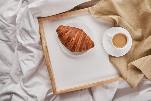 top view of fresh croissant with coffee on wooden tray in bed at morning - Photo, Image