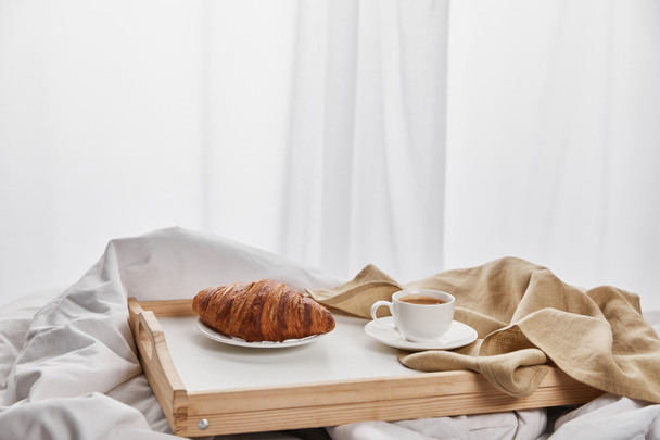 fresh croissant with coffee in cup on wooden tray in bed at morning - Фото, зображення